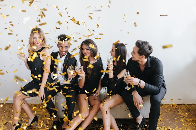 Free photo joyful students celebrating vacation with confetti and chilling on sofa