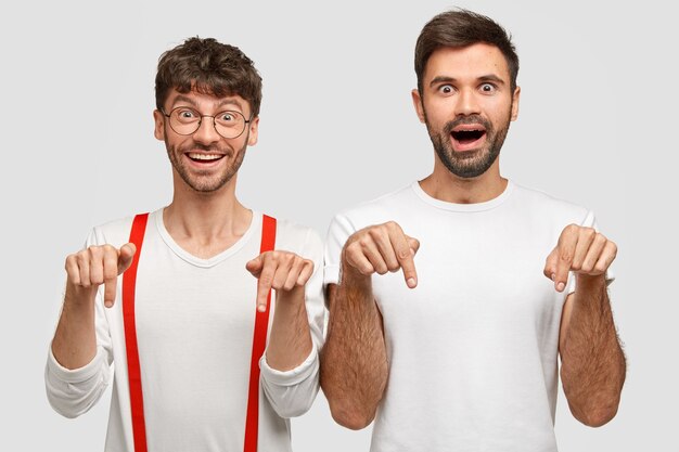 Joyful successful man colleagues or friends have happy expression, point down with index fingers, dressed in white clothes