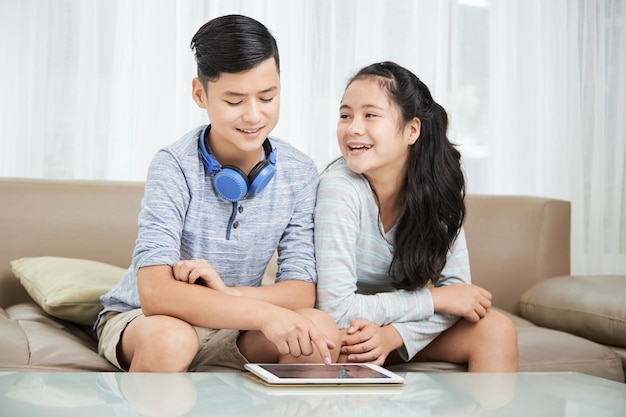 Joyful teenage brother and sister watching videos on tablet computer after school