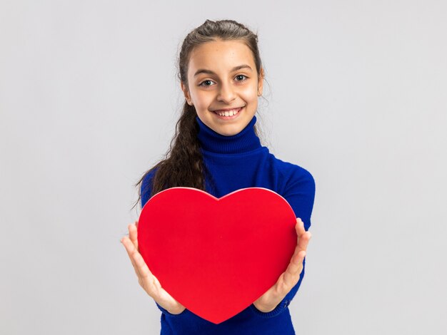 Joyful teenage girl stretching out heart shape towards camera looking at front isolated on white wall with copy space