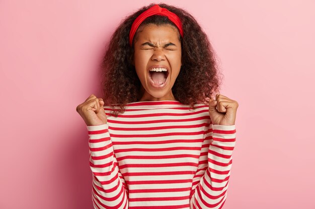 縞模様の赤いセーターでポーズをとって巻き毛のうれしそうな10代の少女