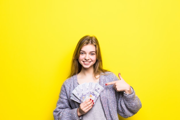 Joyful teenage girl with dollars in her hands pointed on them isolated