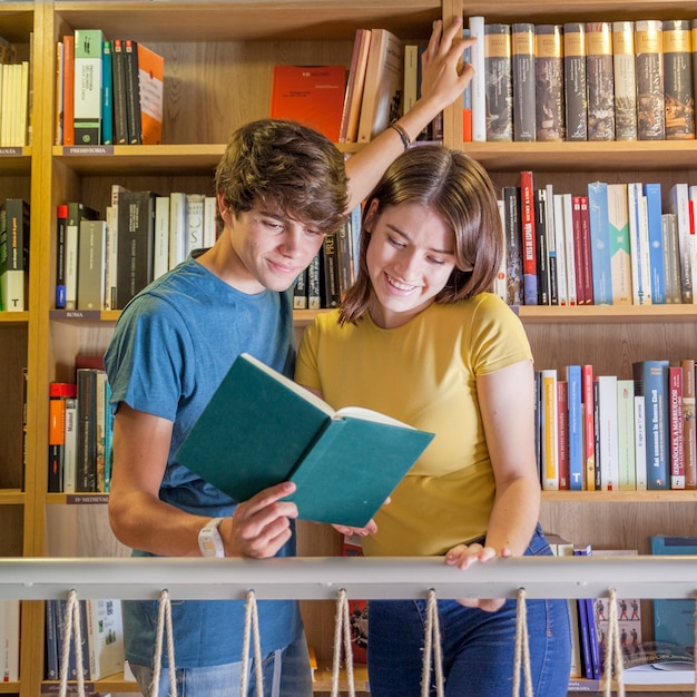 Joyful teenagers reading book in library
