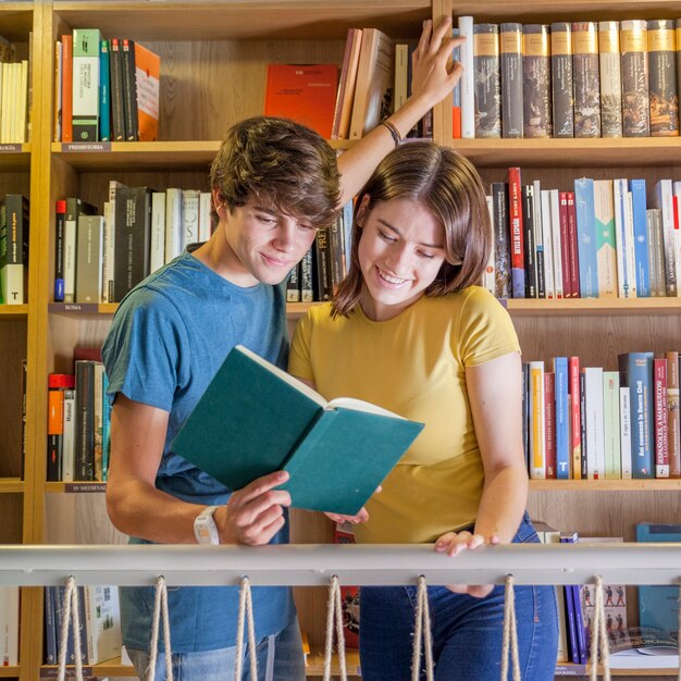 Joyful teenagers reading book in library