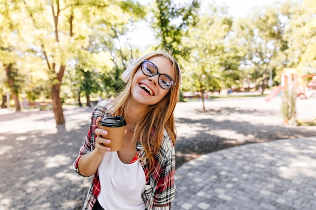 Joyful white girl in glasses expressing positive emotions in park. Caucasian lady enjoying outdoor.