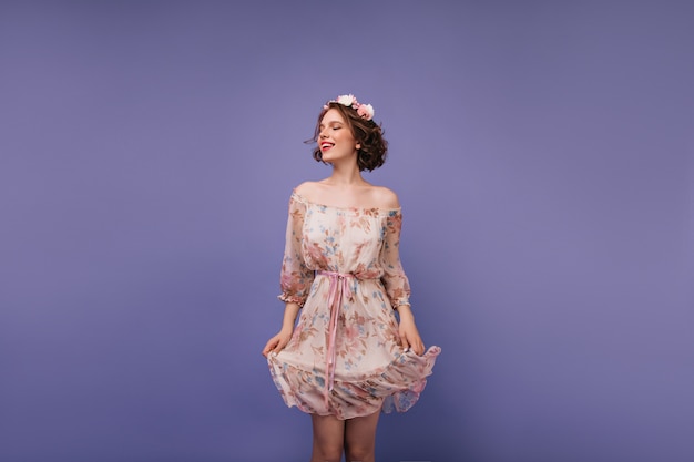 Joyful white girl playing with her romantic dress. magnificent curly lady with flowers on  head.