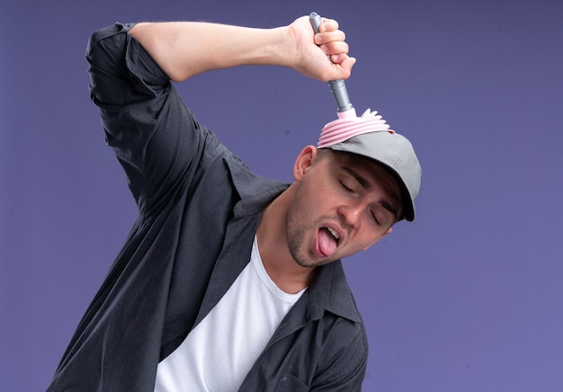 Free photo joyful with closed eyes young handsome cleaning guy wearing t-shirt and cap holding plunger on head isolated on purple wall