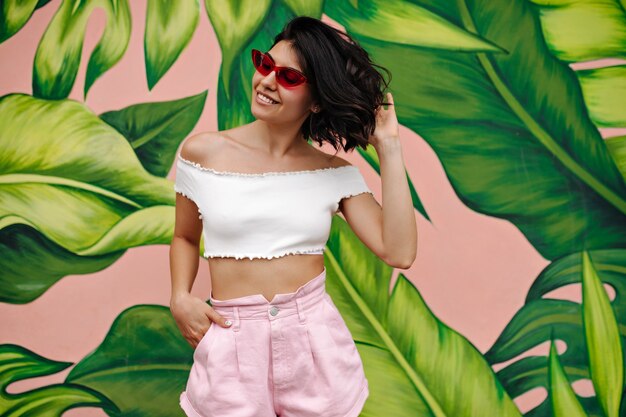 Joyful woman in pink shorts standing near colorful graffiti