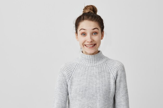 Joyful woman posing  in casual grey with big smile. Brunette female  producer with hair in bun shining with happiness. Media concept