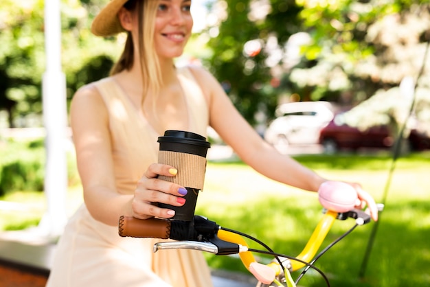 Joyful woman riding bicycle with coffee