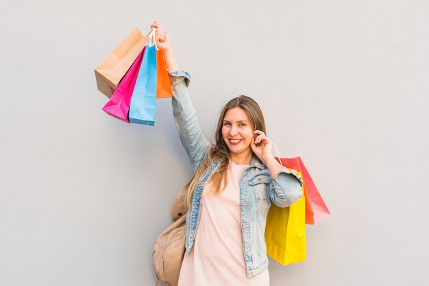 Joyful woman standing with bright shopping bags at light wall