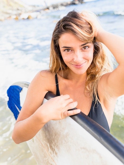 海でサーフボードと立っているうれしそうな女性
