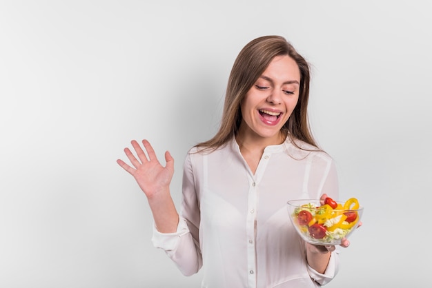 Foto gratuita donna allegra che sta con l'insalata di verdure in ciotola