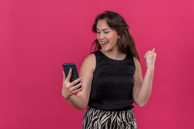 Joyful woman wearing black undershirt listen music from phone on pink wall