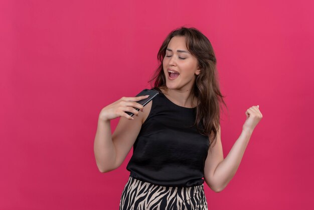 Joyful woman wearing black undershirt listen music from phone on pink wall