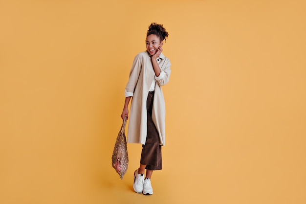 Joyful woman in white sneakers holding string bag