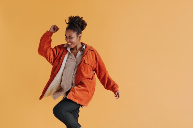 Joyful woman in windbreaker dancing on yellow wall