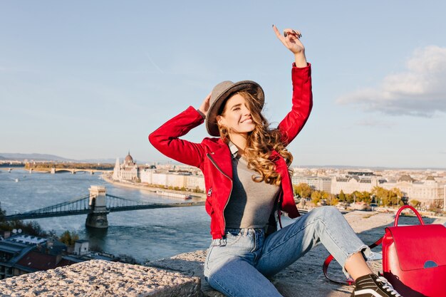 Joyful woman with light-brown hair happy waving hands while posing on city background