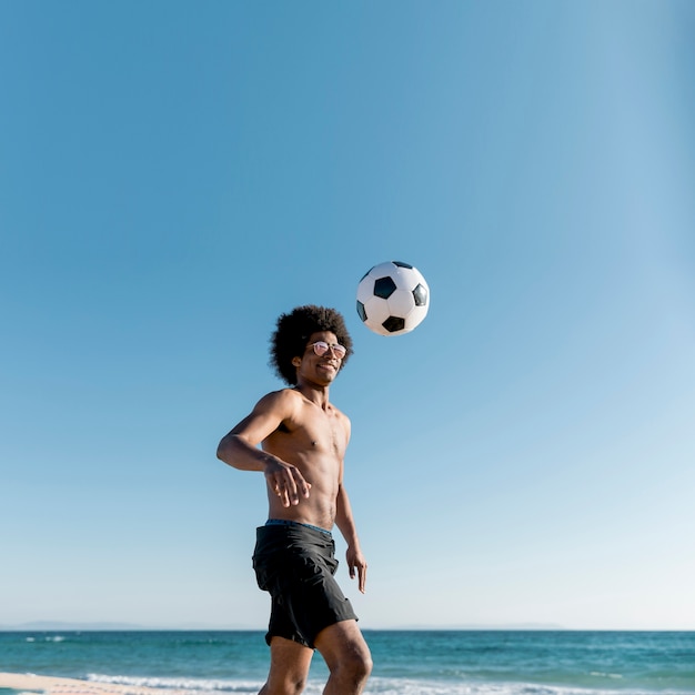 Радостный молодой афроамериканец спортсмен играет в футбол на берегу моря