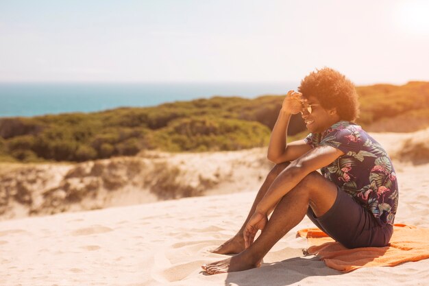 Joyful young African American male sitting by seacoast