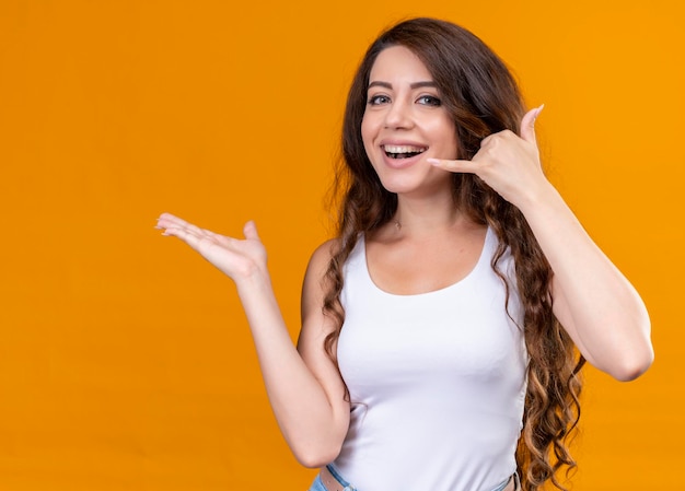 Free photo joyful young beautiful girl doing call sign and showing empty hand on isolated orange space