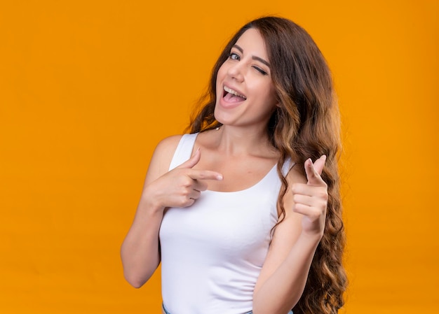 Joyful young beautiful girl doing you gesture and winking on isolated orange space with copy space