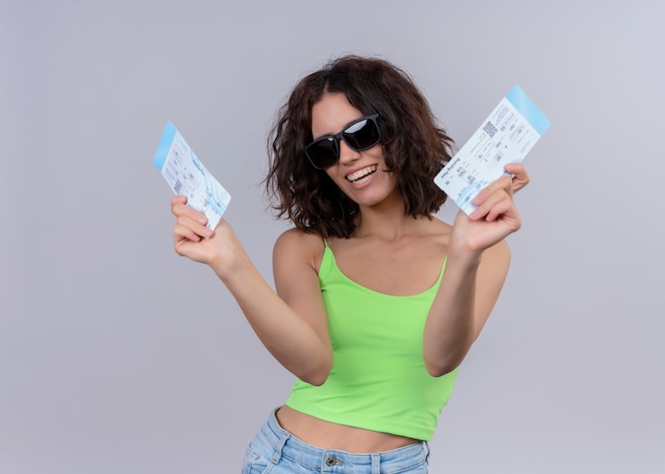 Free Photo joyful young beautiful traveler woman wearing sunglasses and holding airplane tickets on isolated white wall