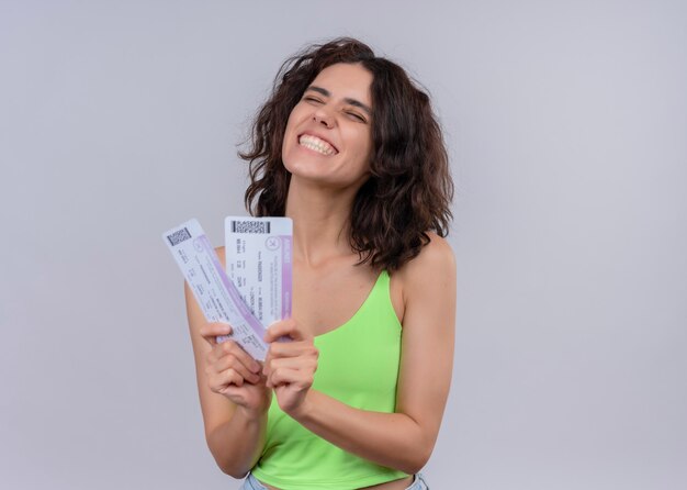 Joyful young beautiful woman holding airplane tickets on isolated white wall with copy space