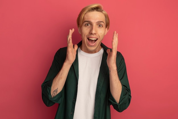 Joyful young blonde guy wearing green t-shirt holding hands around face