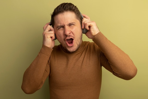 Free photo joyful young blonde handsome man wearing and grabbing headphones enjoying music