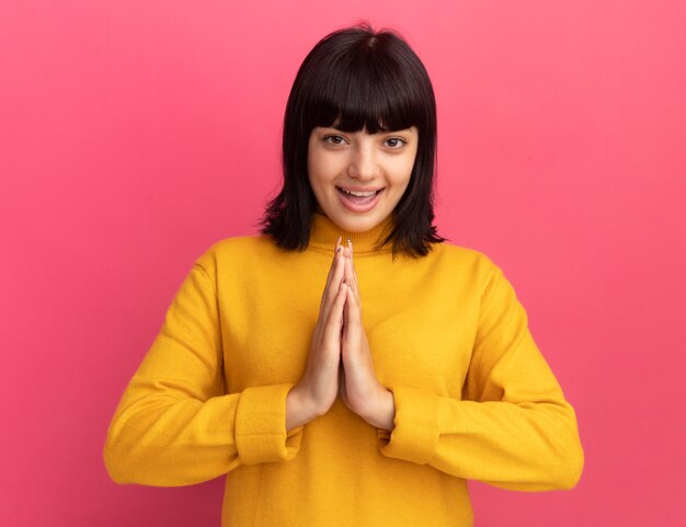 Joyful young brunette caucasian girl holds hands together on pink