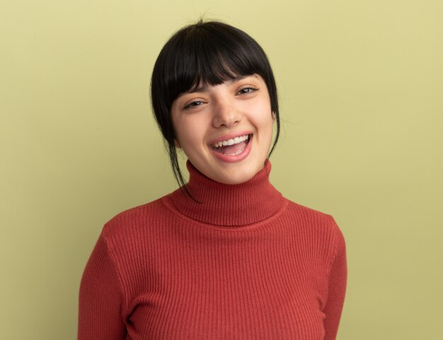 Joyful young brunette caucasian girl  isolated on olive green wall with copy space