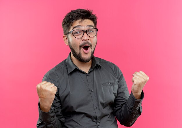 Joyful young businessman wearing glasses showing yes gesture isolated on pink background