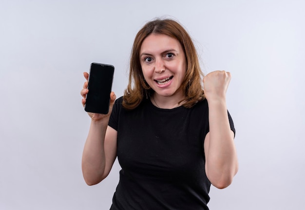 Joyful young casual woman holding mobile phone and raising fist on isolated white space