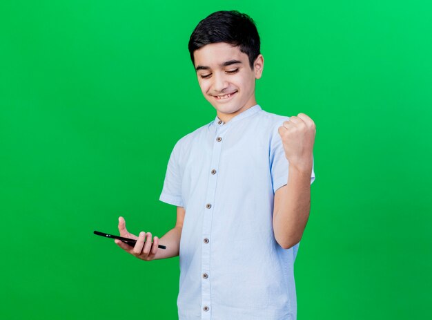 Free photo joyful young caucasian boy holding mobile phone doing yes gesture isolated on green wall with copy space