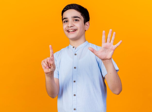 Joyful young caucasian boy looking at camera showing six with hands isolated on orange background with copy space