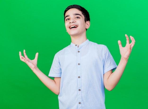 Joyful young caucasian boy showing empty hands  isolated on green wall