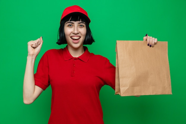 Joyful young caucasian delivery girl holding food packaging and keeping her fist up