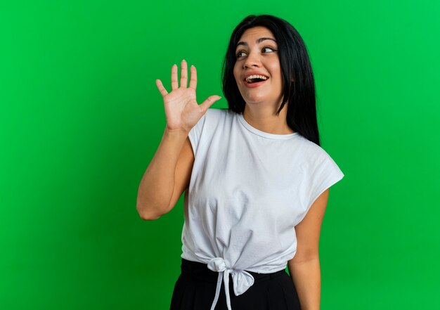 Joyful young caucasian girl stands with raised hand looking at side 