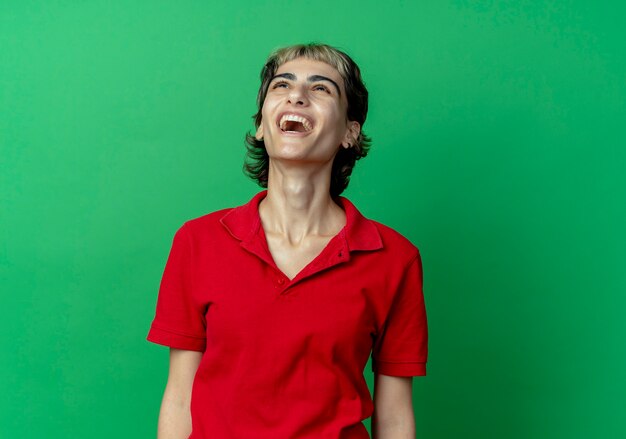 Joyful young caucasian girl with pixie haircut looking up isolated on green background with copy space