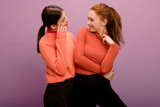 セーターとズボンのうれしそうな若い白人の女の子は紫色の背景でお互いを見てライフスタイルのさまざまな感情レジャーコンセプト