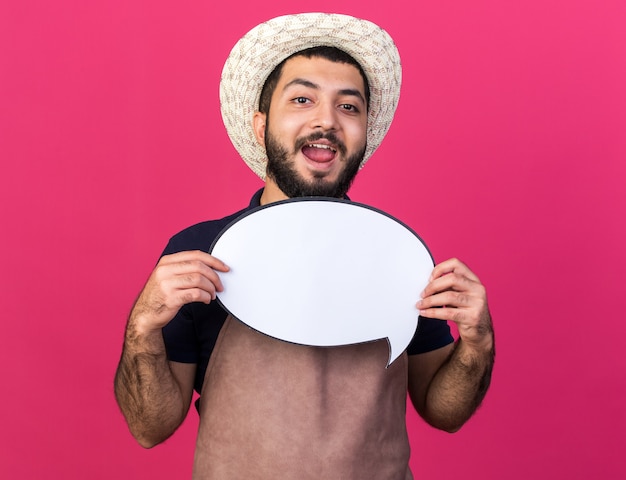 joyful young caucasian male gardener wearing gardening hat holding speech balloon isolated on pink wall with copy space