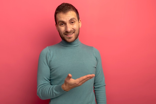 Joyful young caucasian man looking at camera pointing at side with hand isolated on crimson background with copy space