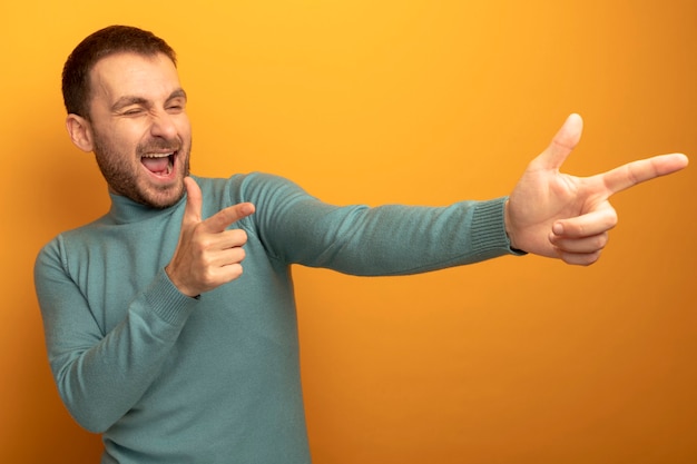 Joyful young caucasian man winking looking at side doing you gesture isolated on orange wall