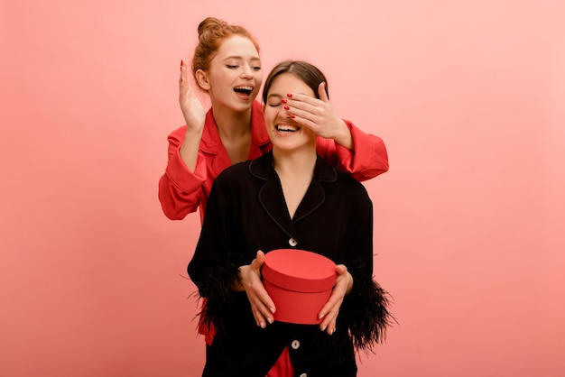 Free photo joyful young caucasian woman closes her eyes to friend sitting on chair making surprise on pink background concept of pleasant emotions