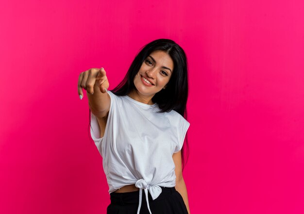 Joyful young caucasian woman looks and points at camera