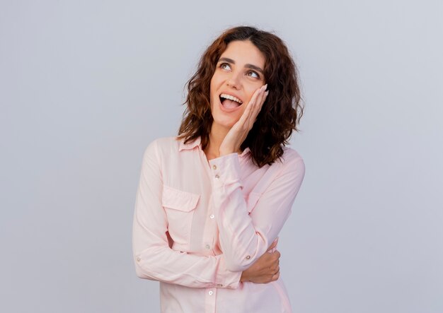 Joyful young caucasian woman puts hand on face and looks up