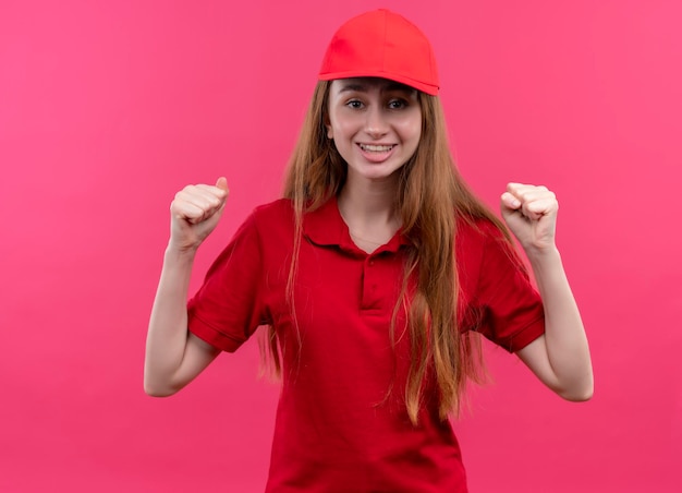 Gioiosa giovane ragazza di consegna in uniforme rossa con i pugni alzati su uno spazio rosa isolato