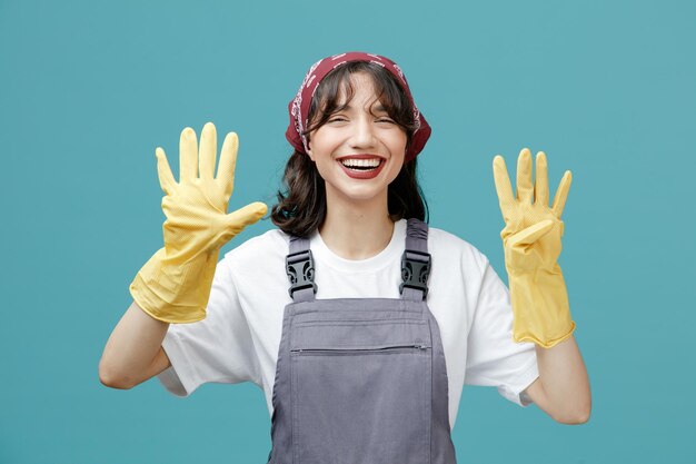 유니폼 반다나와 고무 장갑을 끼고 파란 배경에 손이 격리된 9개의 카메라를 보고 있는 즐거운 젊은 여성 청소부