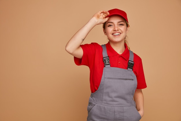 ポケットをつかむキャップに手を入れてキャップと制服を着てうれしそうな若い女性建設労働者